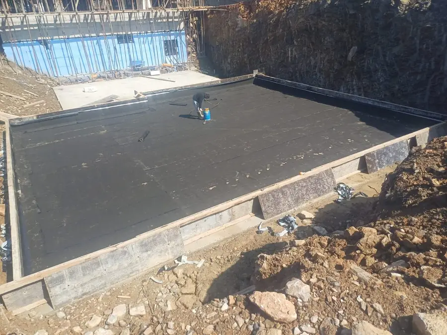 Temel döşemesine serilen siyah bitümlü membran ve ortada pürmüzle ek yeri yapan usta