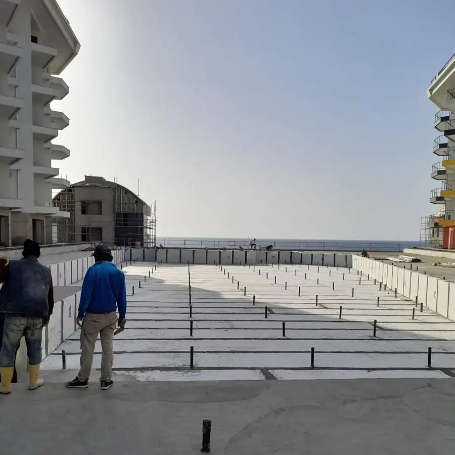 Deniz kıyısındaki iki blok arasında, filiz demirleri çakılı geniş temel platformunda yalıtım öncesi hazırlık