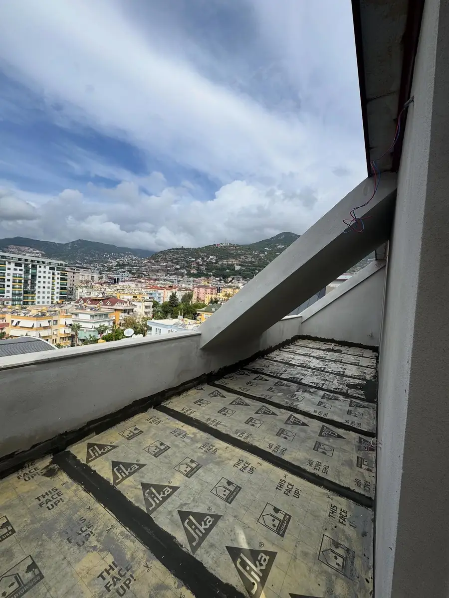 Dar teras balkonda parapet boyunca sıralanmış Sika yalıtım levhaları, arkada şehir ve dağ manzarası