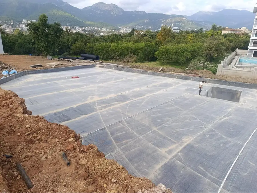 Geniş betonarme platforma serilmiş su yalıtım örtüsü ve kenarlardaki dönüşler, arkada dağ manzarası