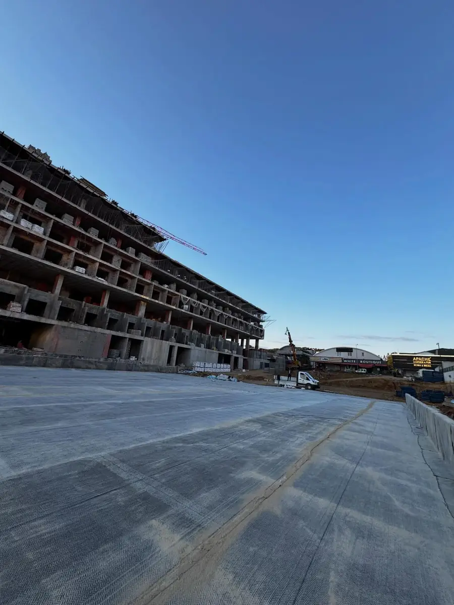 Kaba inşaat halindeki otel bloğunun önünde geniş beton platforma serilmiş gri koruma örtüsü